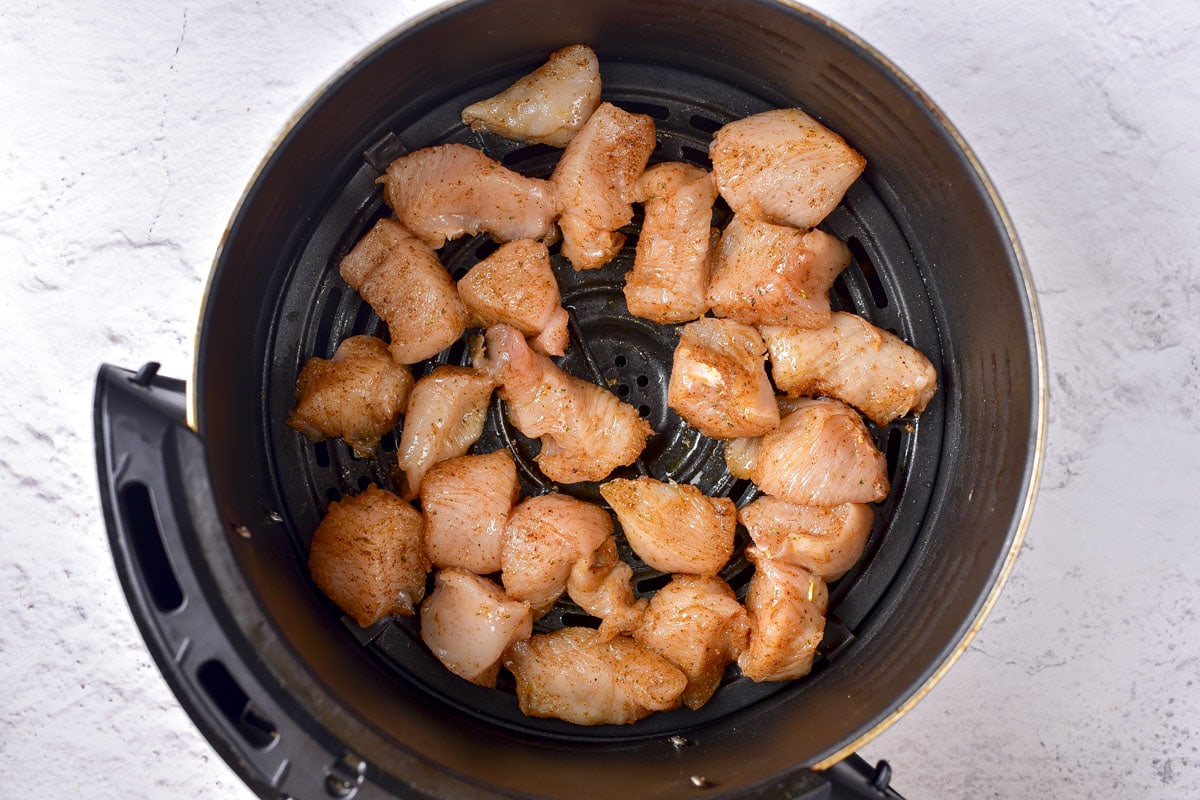 raw chicken pieces in round black air fryer tray on counter.