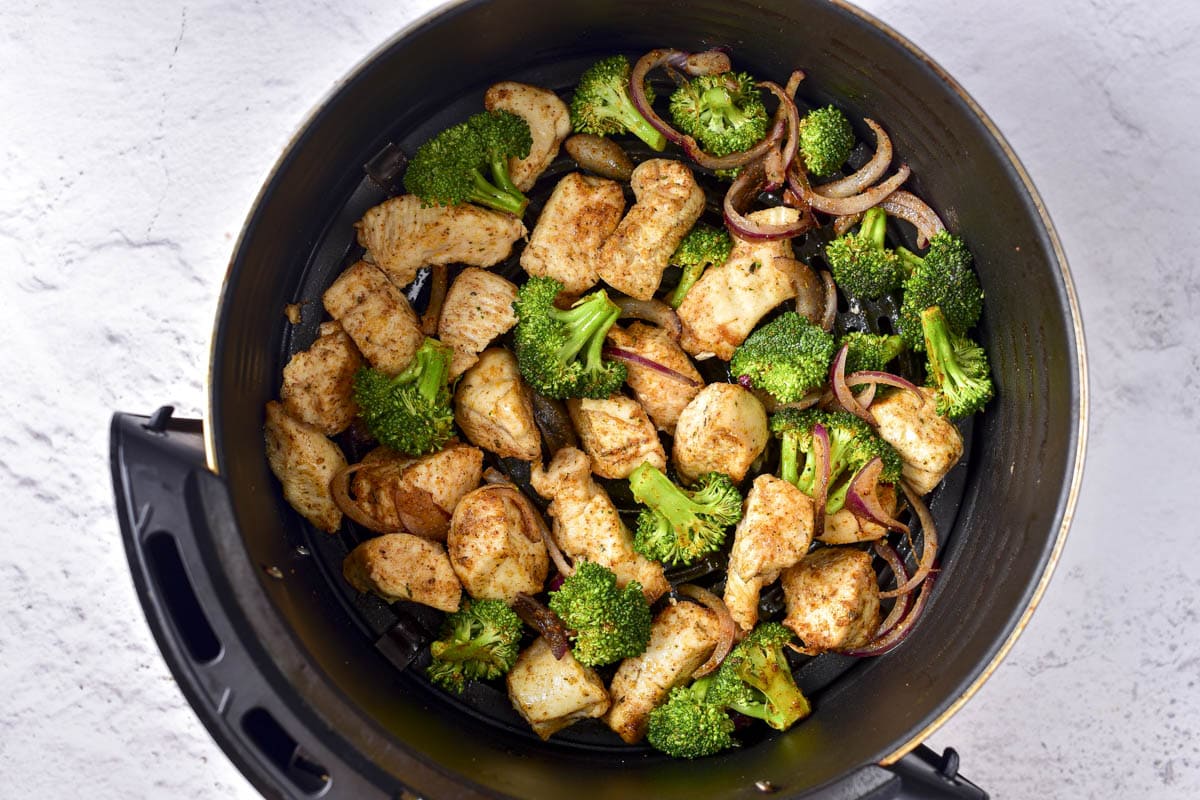 chicken and broccoli cooking together in round black air fryer basket.