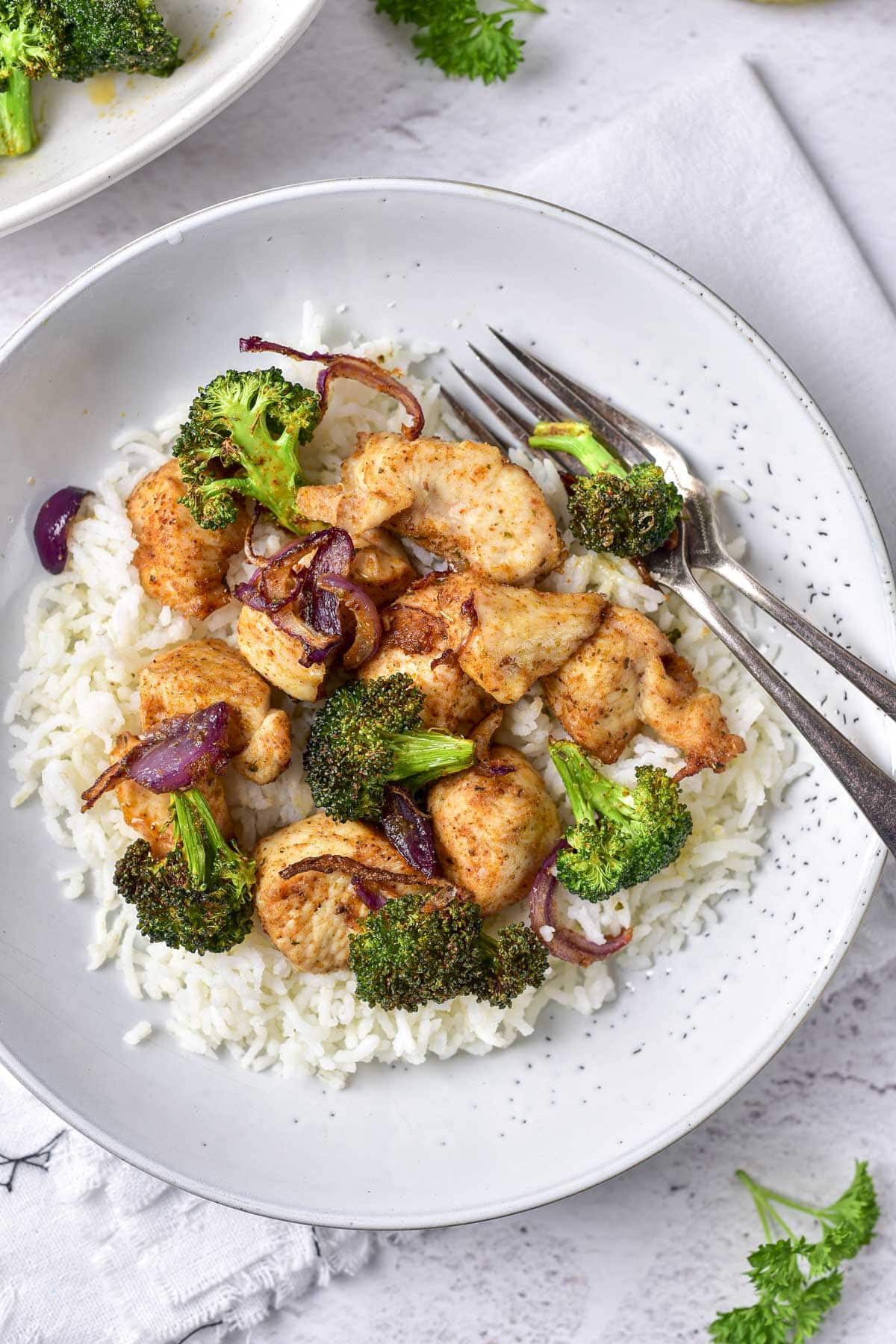 white plate with chicken broccoli and rice with silver forks beside.