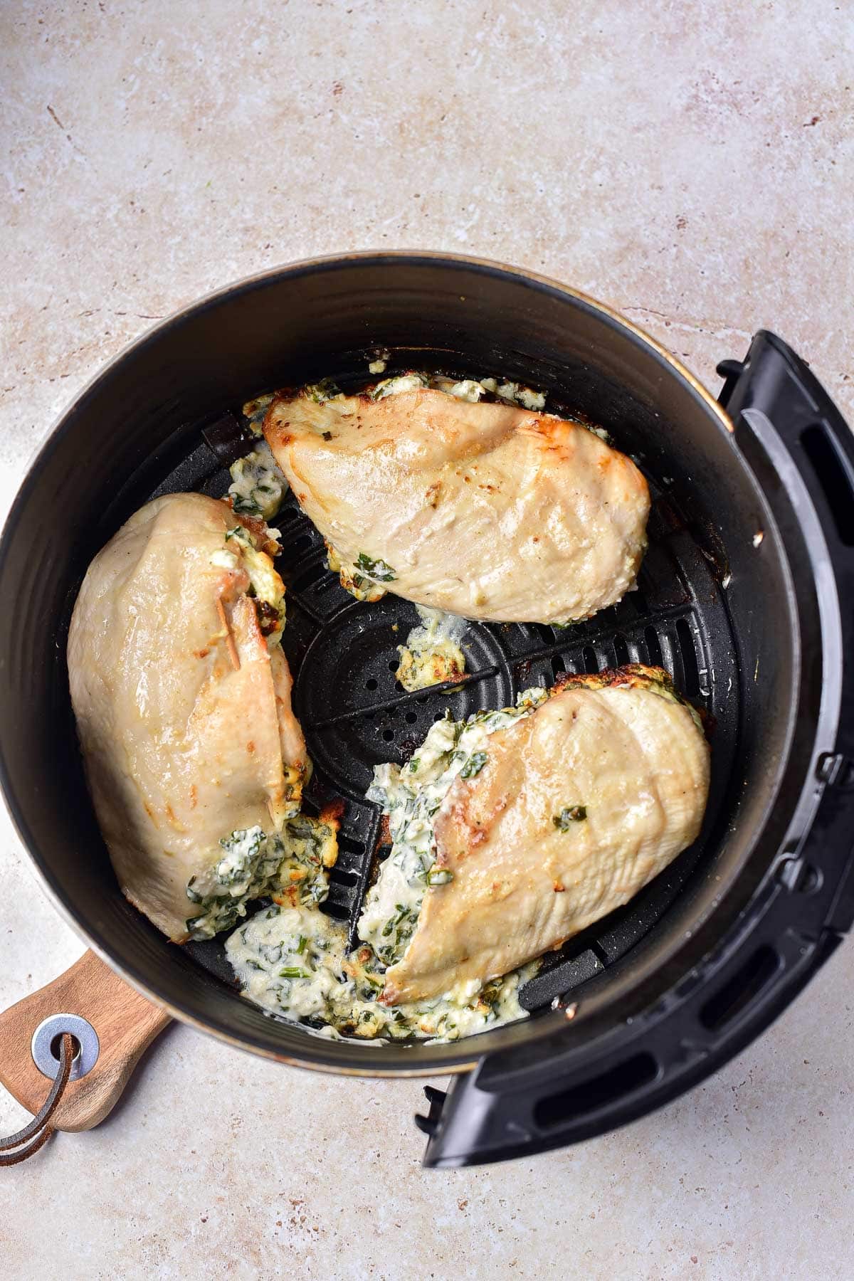 three cooked stuffed chicken breasts in black air fryer tray with filling coming out.