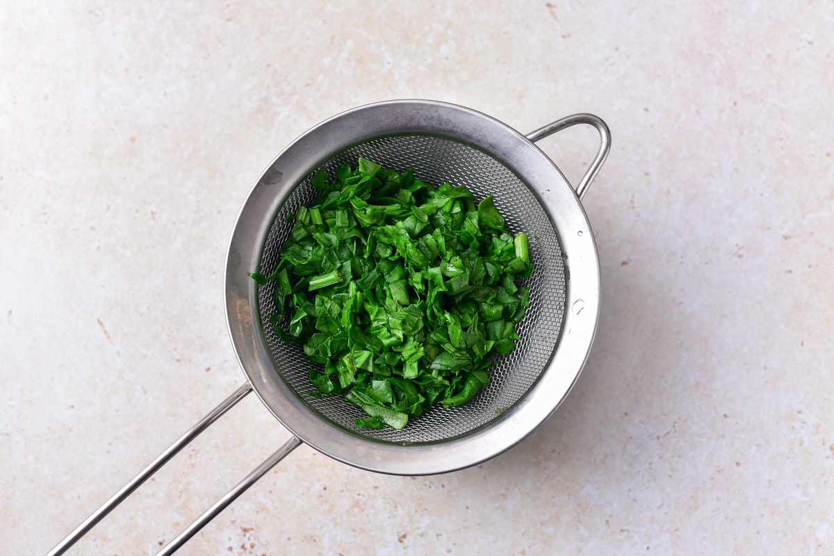 chopped spinach in silver colander sitting on counter top. 