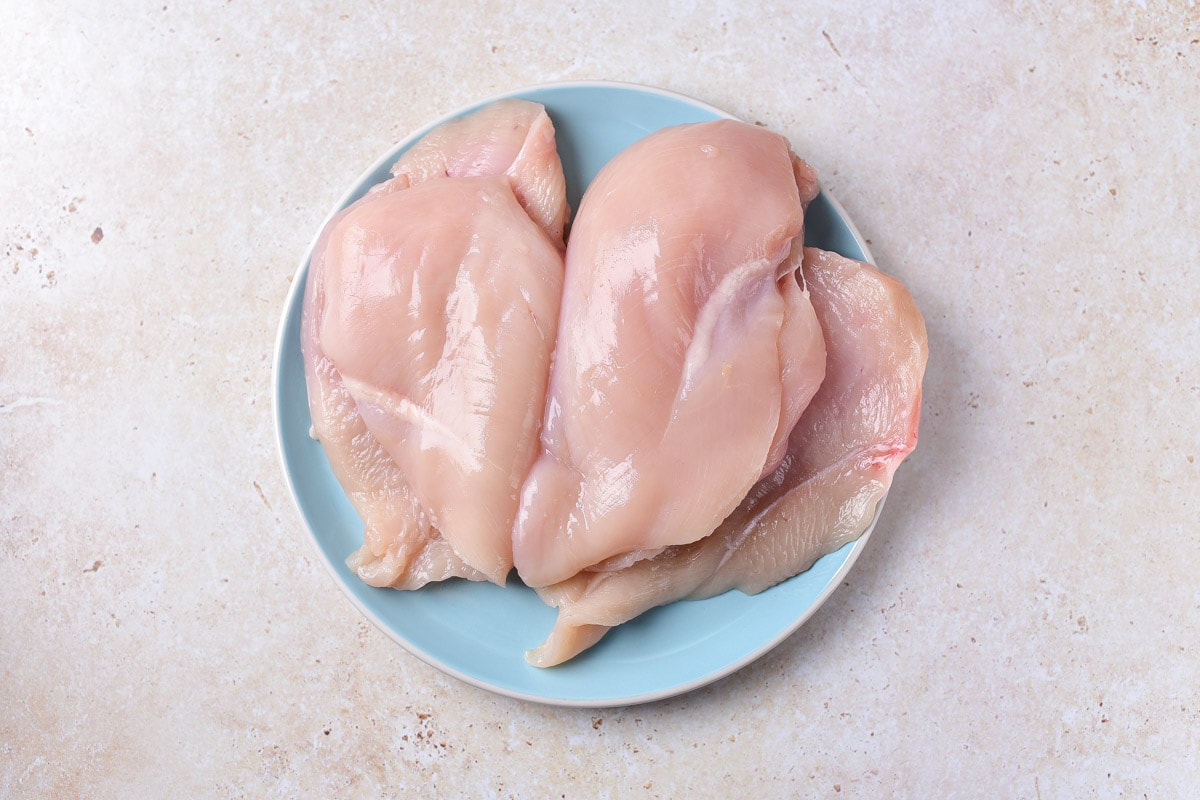 three chicken breasts on blue plate on counter with a cut into them lengthwise.