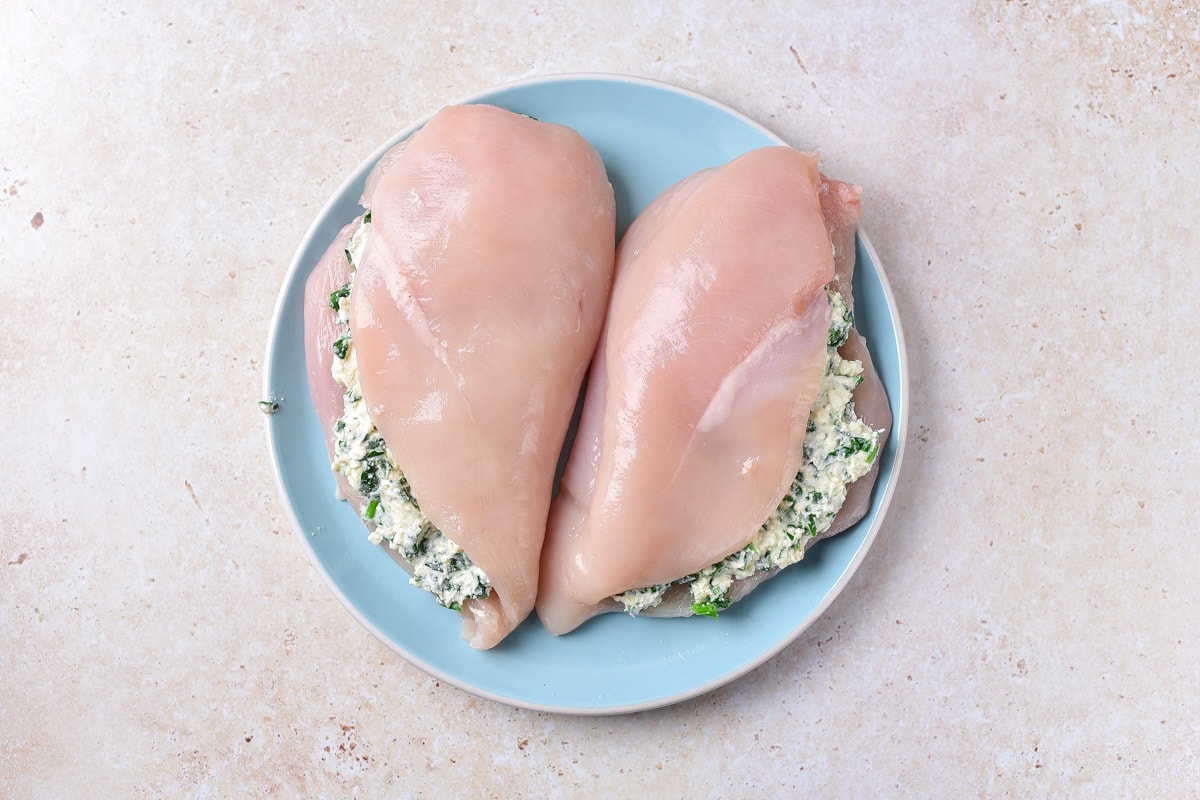 two raw stuffed chicken breasts on blue plate on counter.