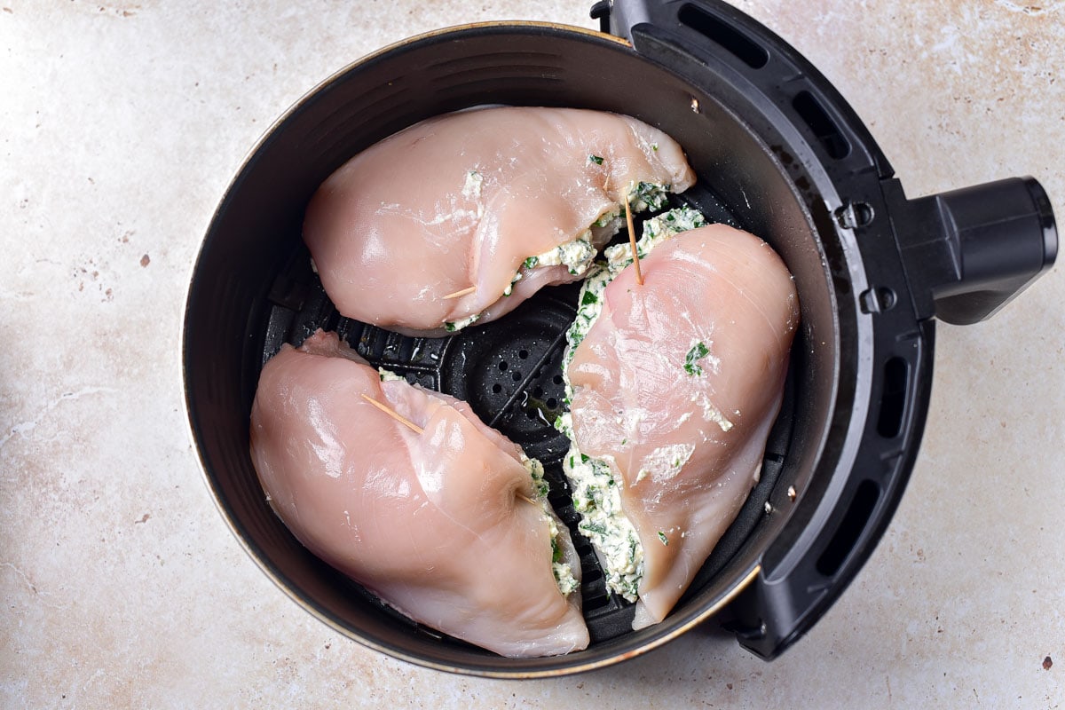 three raw stuffed chicken breasts in round black air fryer tray on counter.