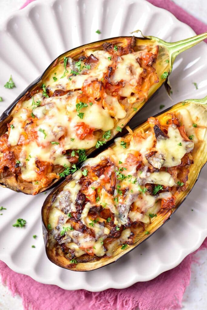 Two stuffed eggplant halved covered in cheese sitting on white plate.