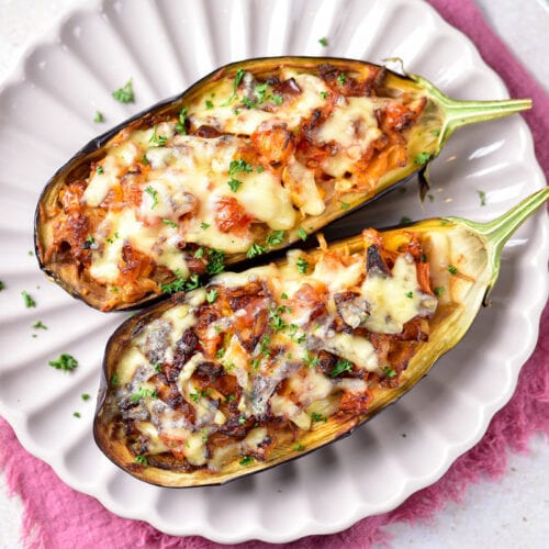 two cooked air fryer eggplant halves covered in cheese on white plate.