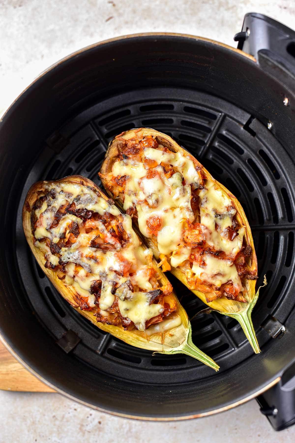two cooked stuffed eggplant halves sitting in round black air fryer tray.