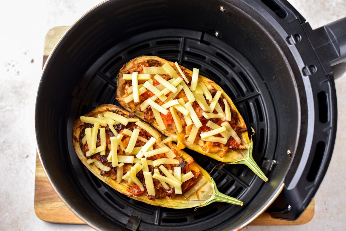 stuffed eggplant halves covered in shredded cheese sitting in round black air fryer tray.
