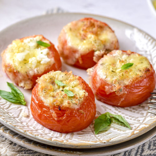 four cooked stuffed tomatoes on plate with forks beside.