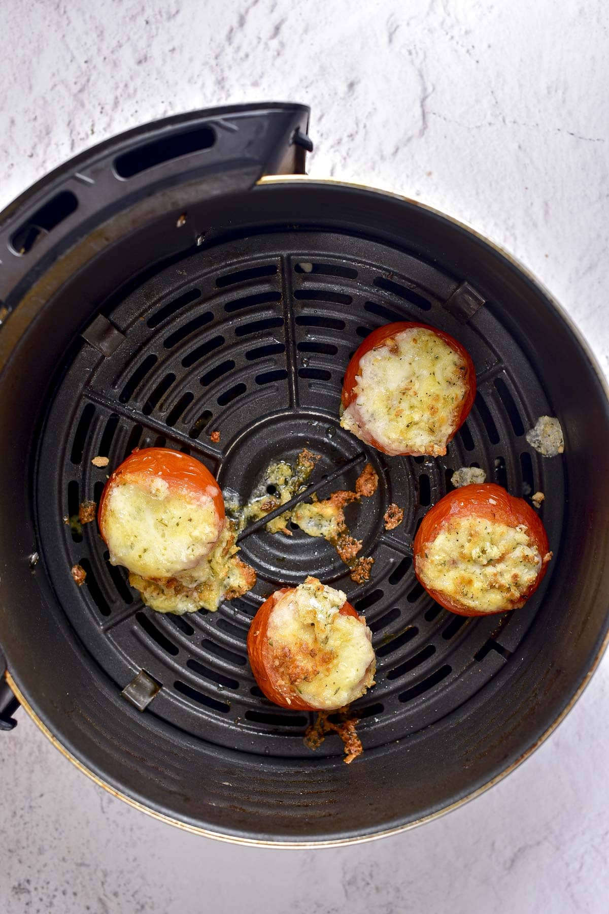 four cooked stuffed tomatoes spilling their stuffing in a black air fryer tray.