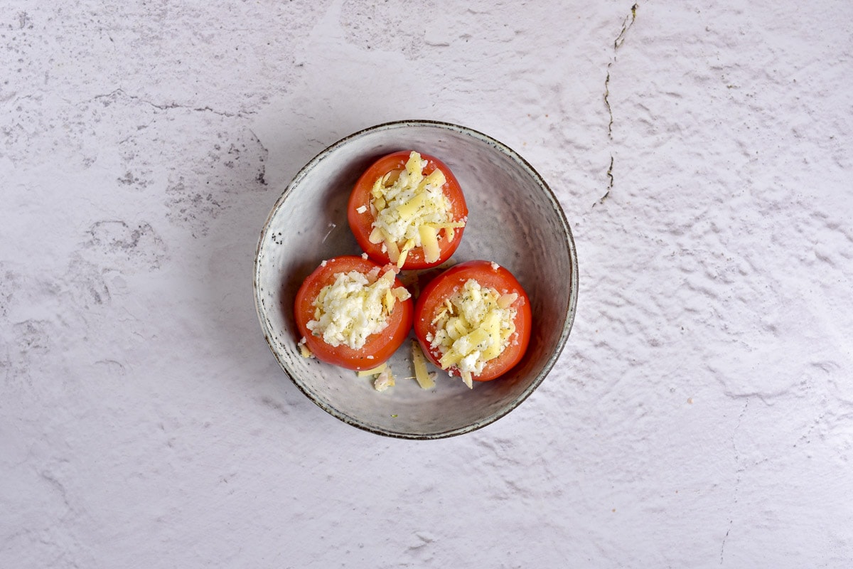 three tomatoes on a plate stuffed with cheese and breadcrumbs.