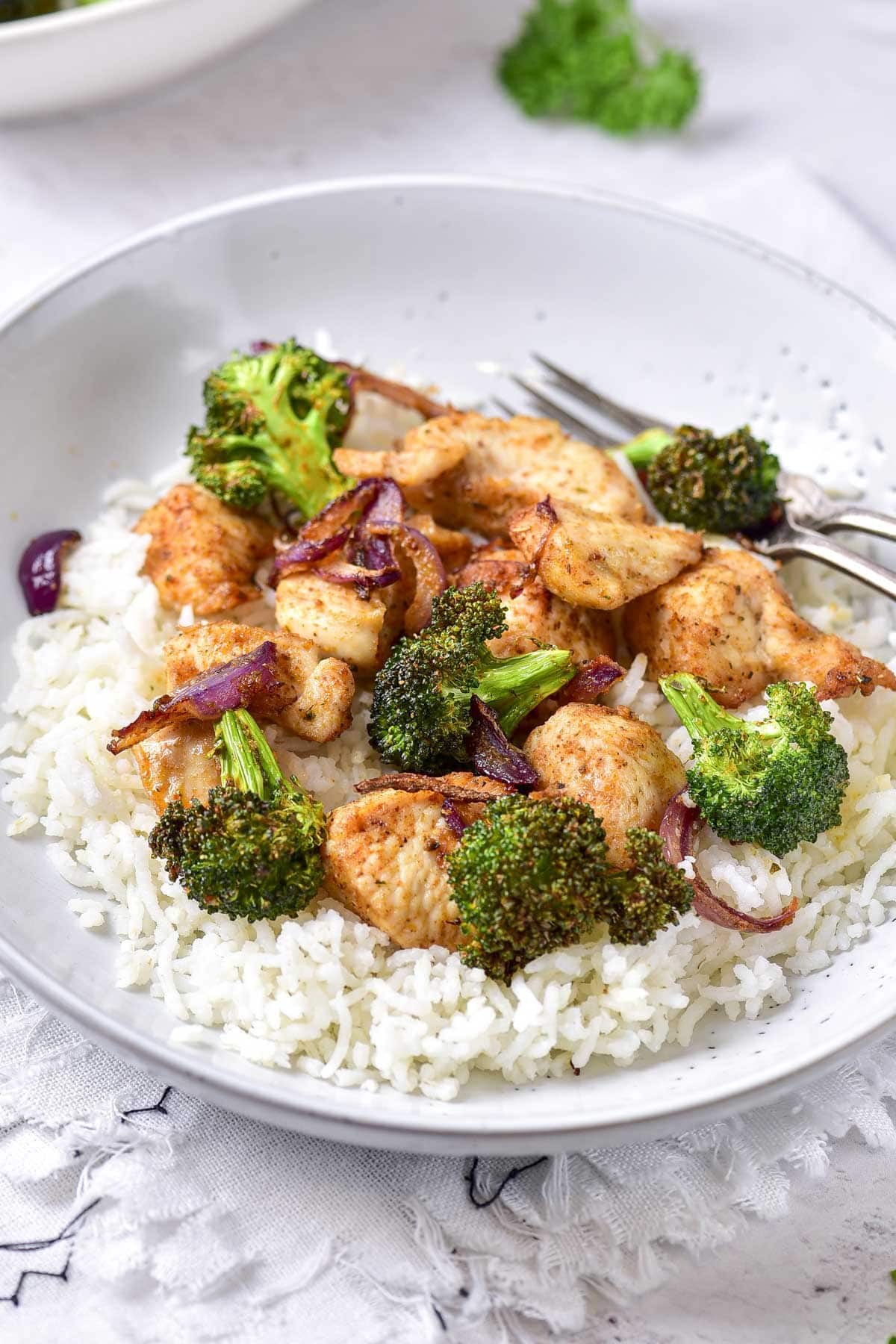 cooked chicken and broccoli on rice on white plate with fork behind.