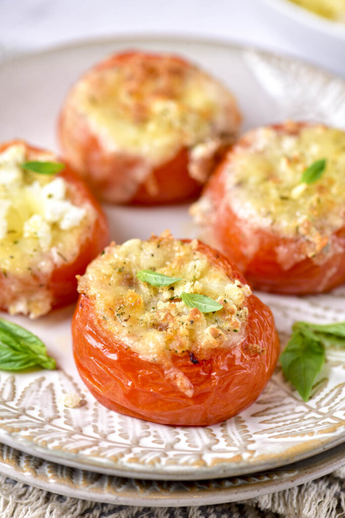 stuffed fried tomatoes sitting on plates with green basil beside.