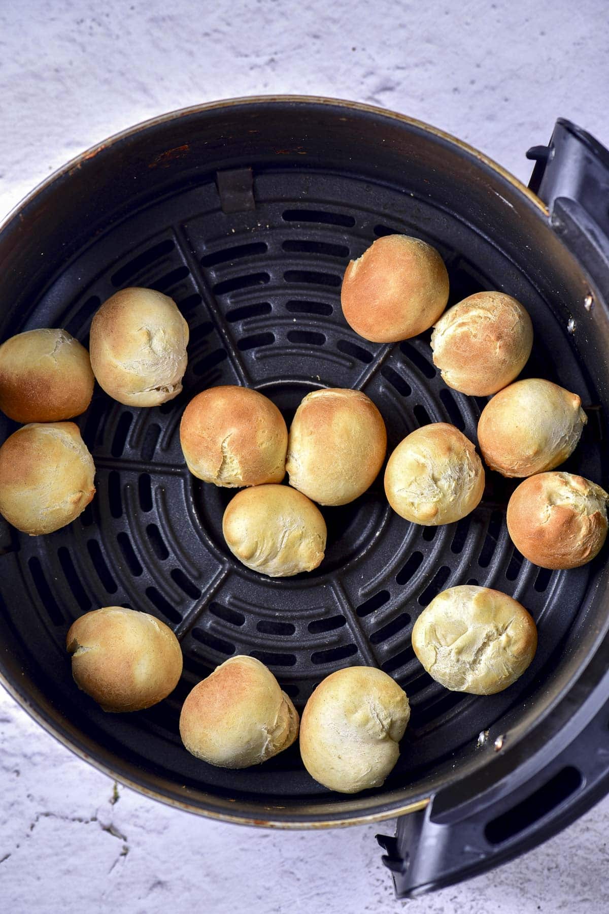 cooked donut holes in round black air fryer tray on counter.
