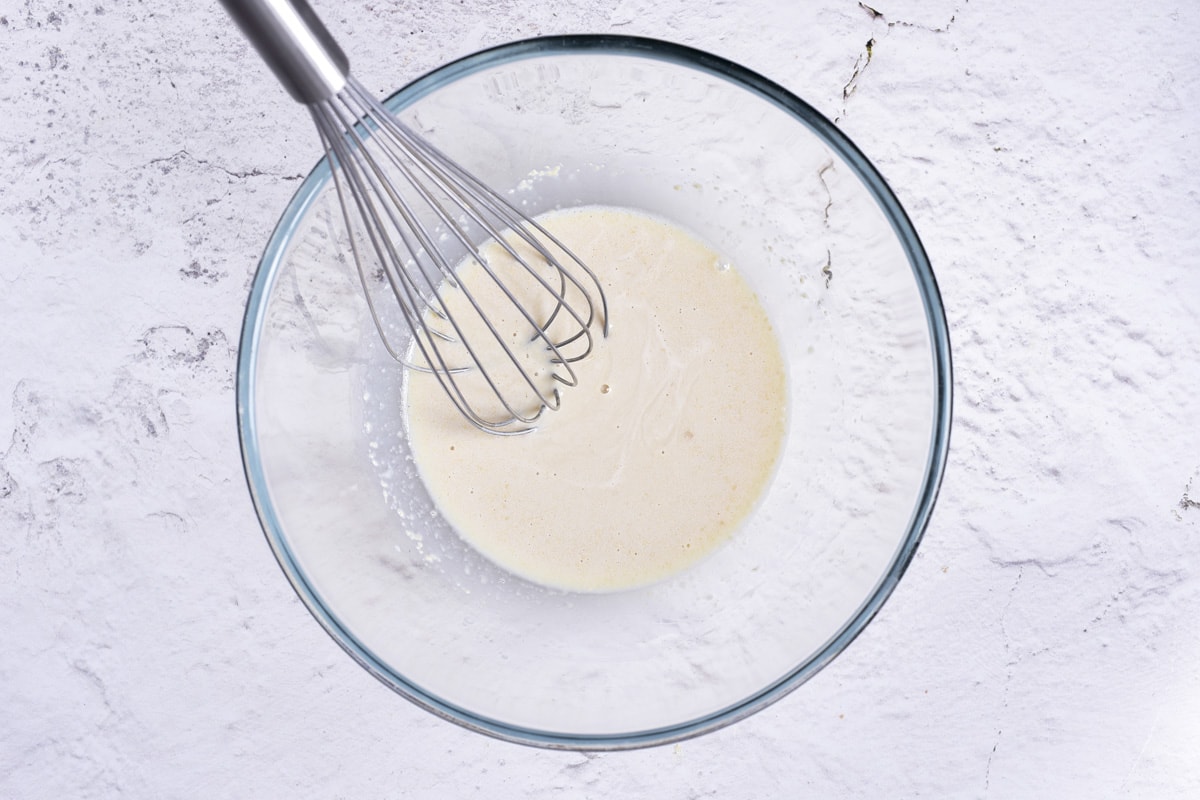 thin batter in clear mixing bowl with silver whisk sticking out.