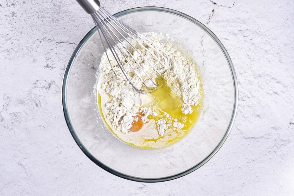 flour and other ingredients in clear mixing bowl with whisk on counter.