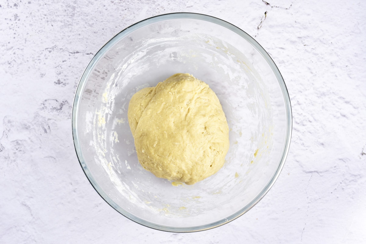 ball of donut dough in clear mixing bowl on counter.