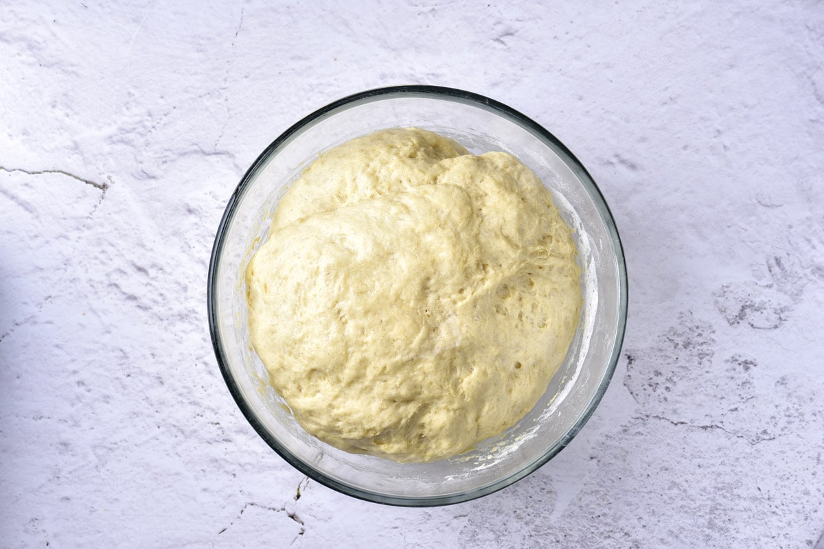 risen ball of dough in clear glass bowl on counter.