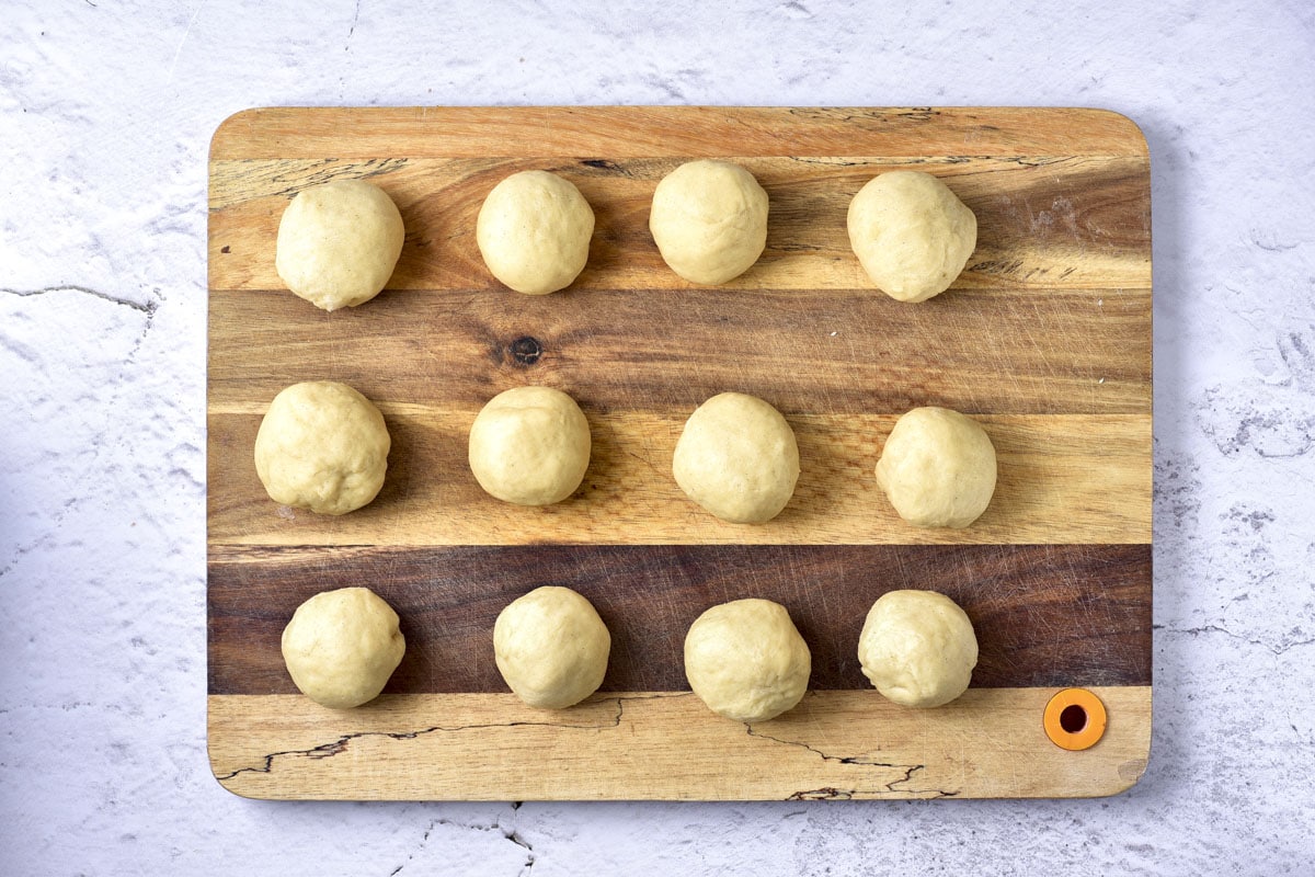 small balls of raw donut dough sitting in rows on wooden cutting board.