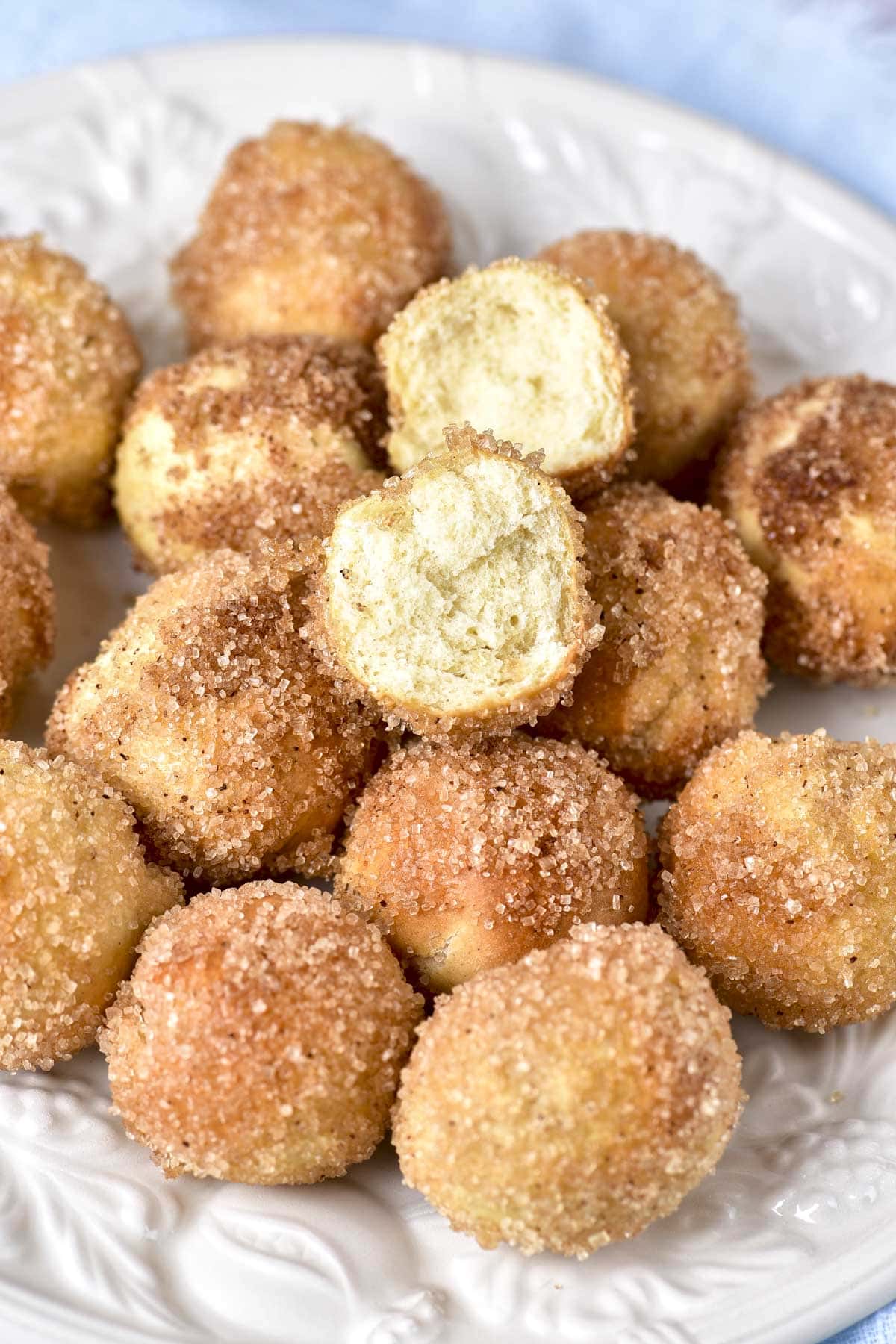 close-up photo of many donut holes covered in cinnamon and sugar on plate, one ripped in half.