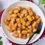 bowl of air fried gnocchi with fork in it sitting on counter with cloth underneath.