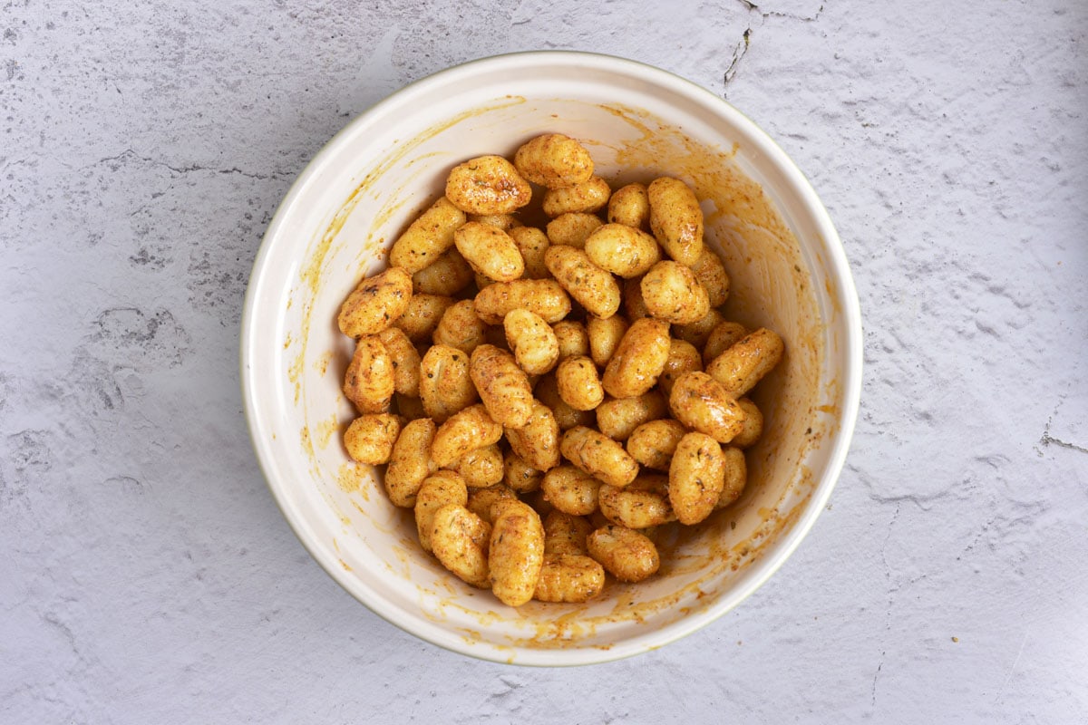 raw gnocchi tossed in oil and spices in white bowl on counter.