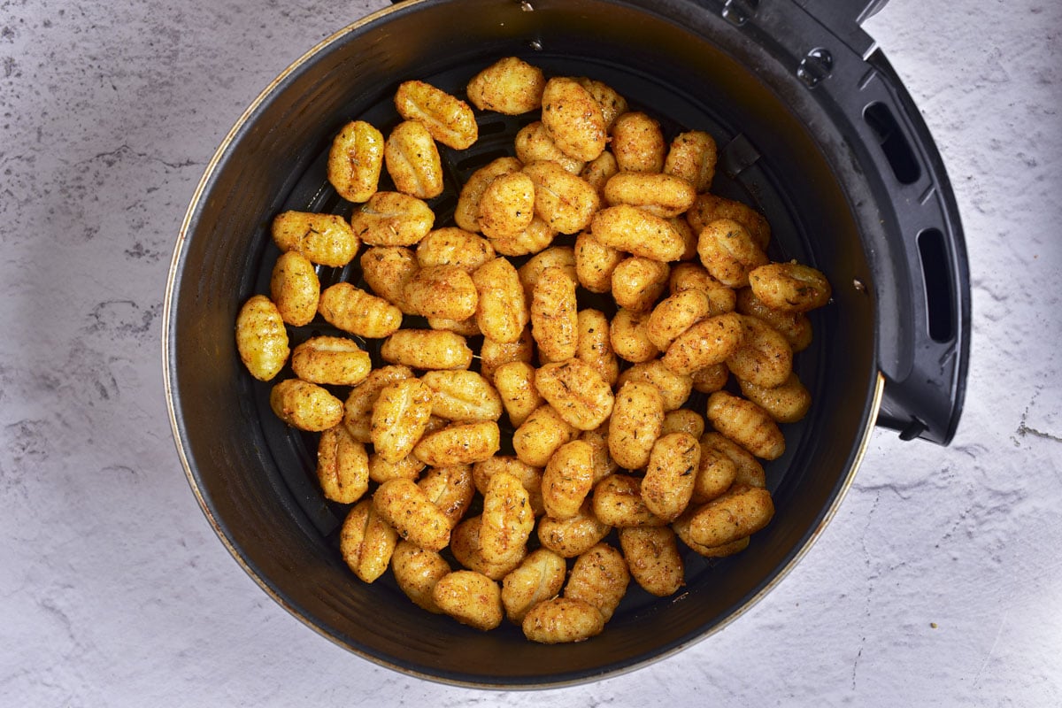 gnocchi covered in spices in round air fryer basket on counter.