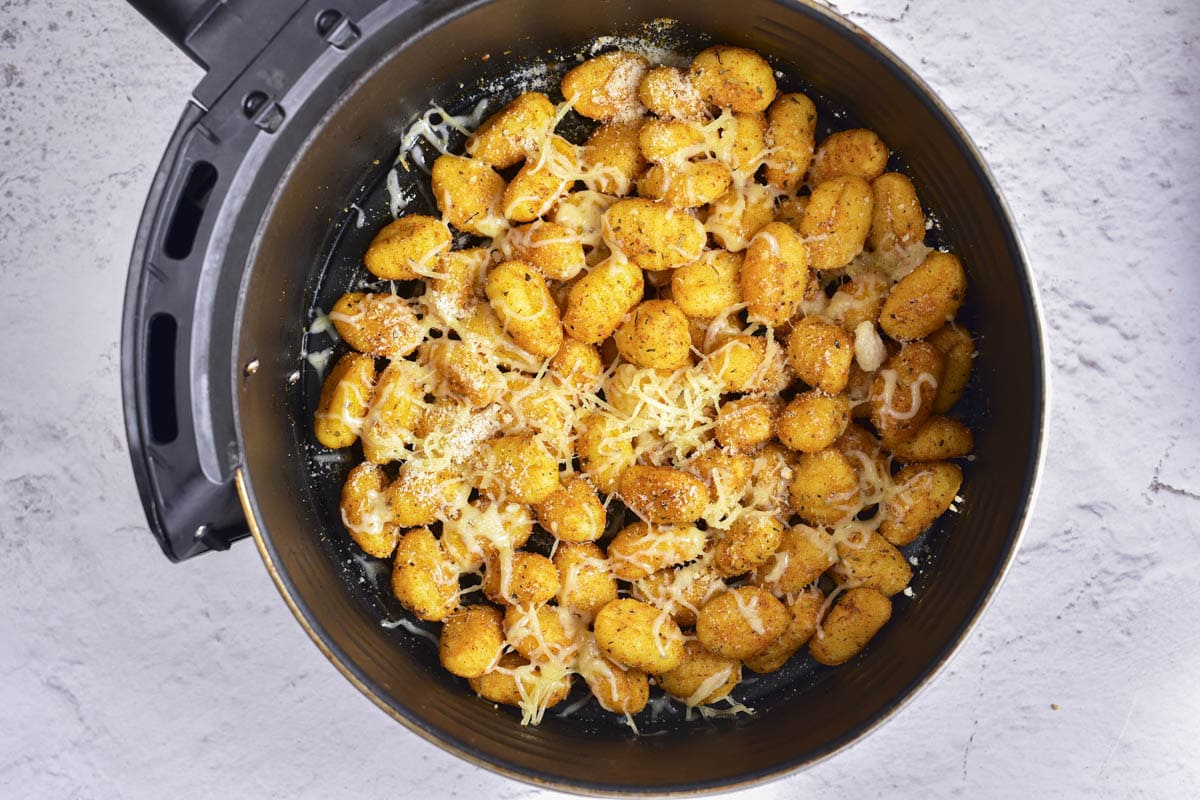 gnocchi in air fryer basket covered in shredded parmesan cheese.