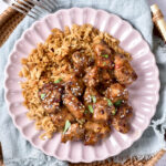 honey garlic chicken pieces sitting on bed of rice on plate.