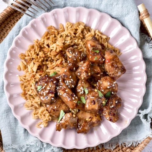 honey garlic chicken pieces sitting on bed of rice on plate.