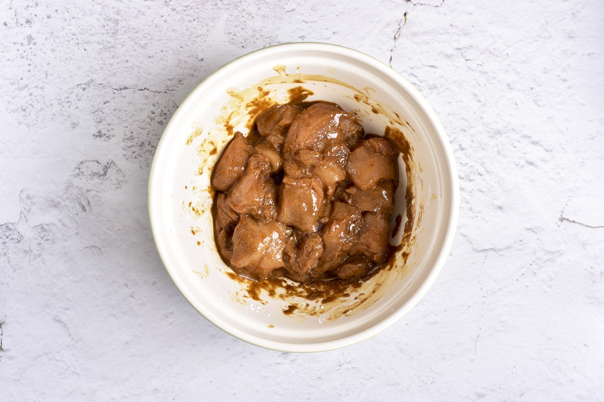 chunks of raw chicken in sauce sitting in white bowl on counter.
