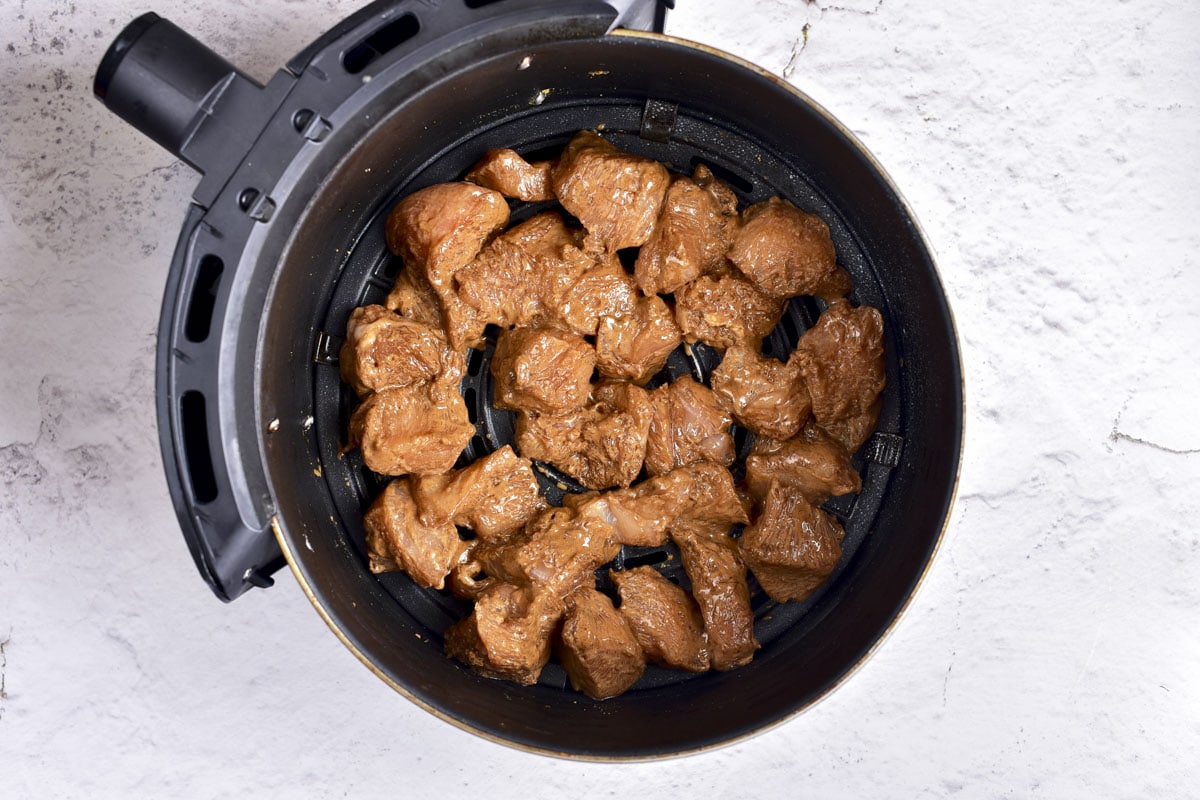 raw honey garlic chicken pieces in round air fryer basket on counter.