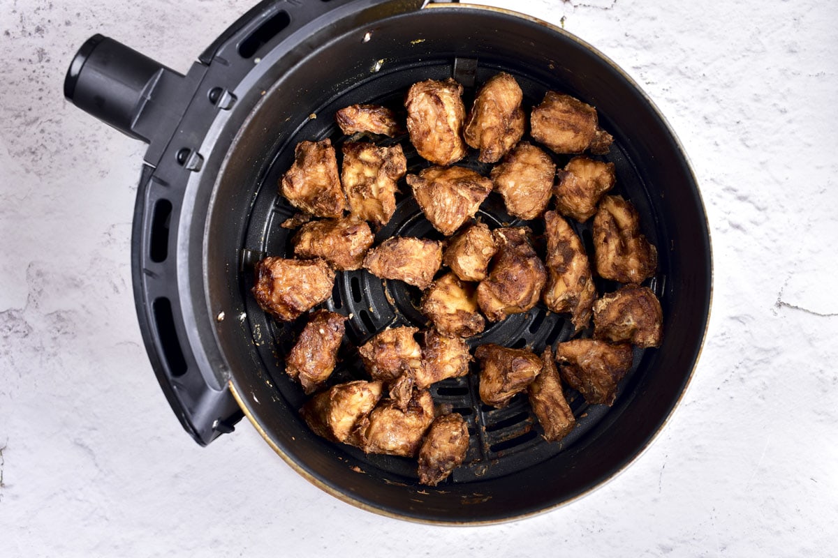 cooked pieces of honey garlic chicken in round black air fryer tray on counter.
