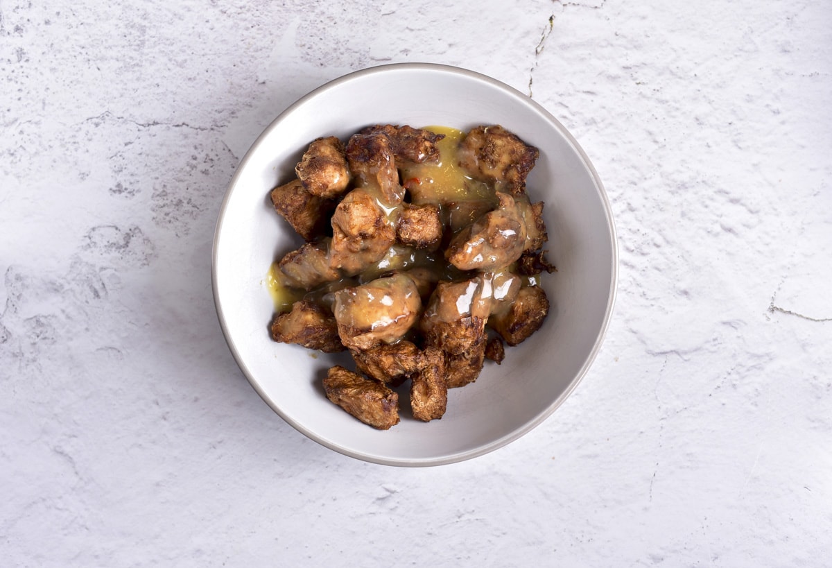 white bowl filled with cooked honey garlic chicken pieces sitting on counter top.