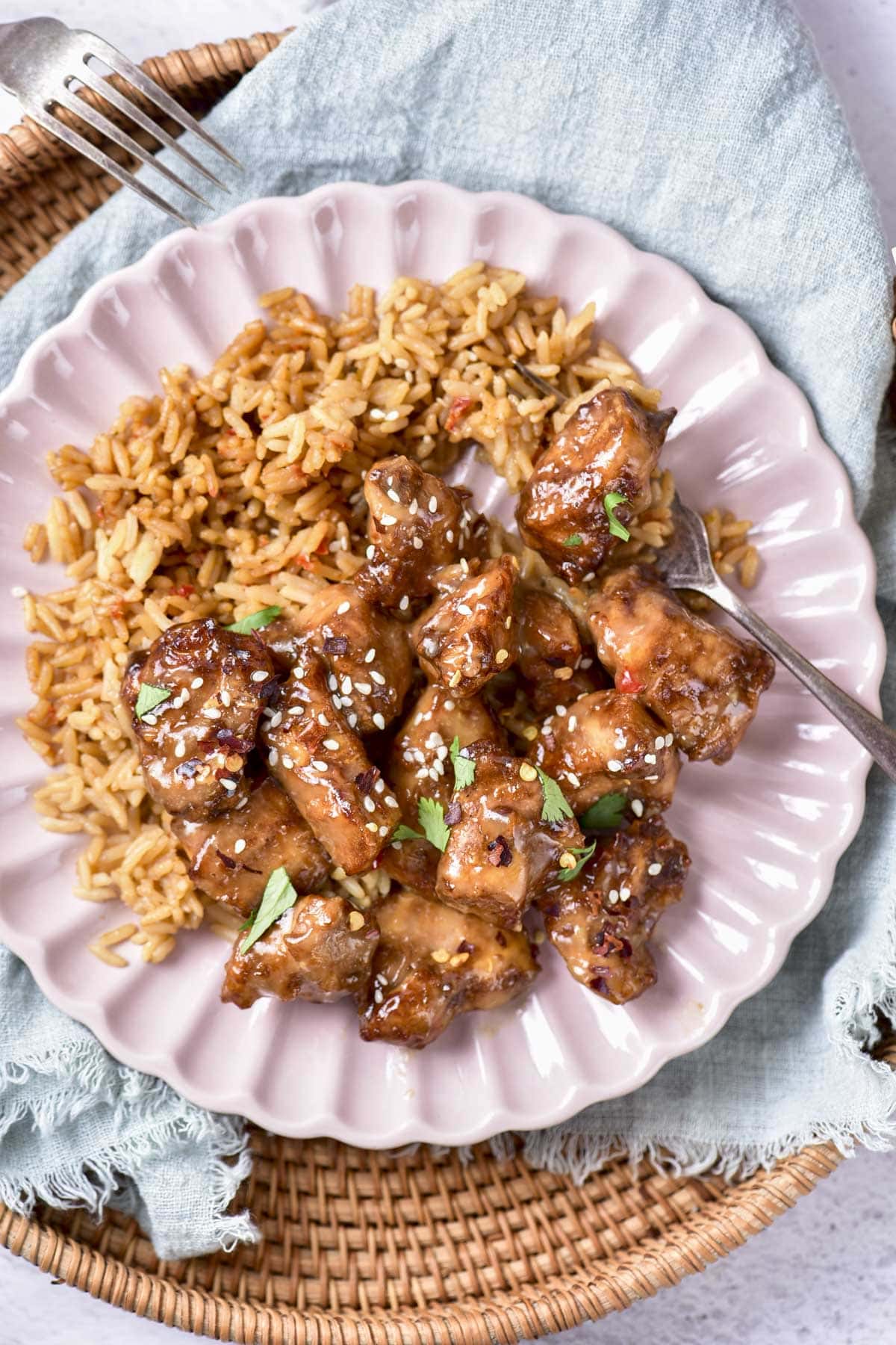 top down view of honey garlic chicken pieces on rice on pink plate with fork beside.