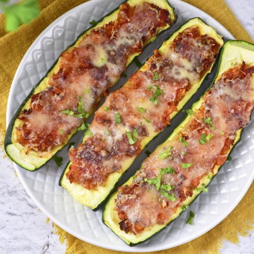 three stuffed zucchinis on white plate with yellow cloth underneath.