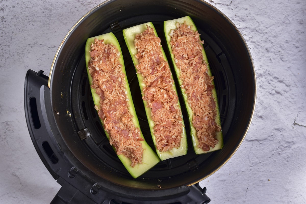 raw stuffed zucchini boats in round black air fryer basket.