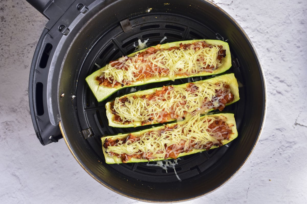 stuffed zucchini boats in air fryer basket with shredded cheese on top.