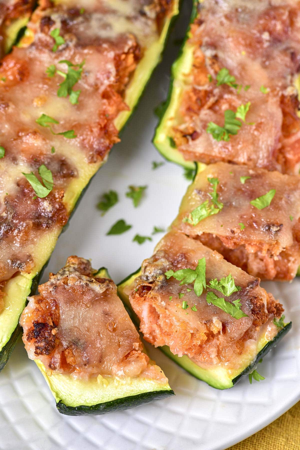 cooked stuffed zucchini boats cut into pieces on white plate with parsley around.