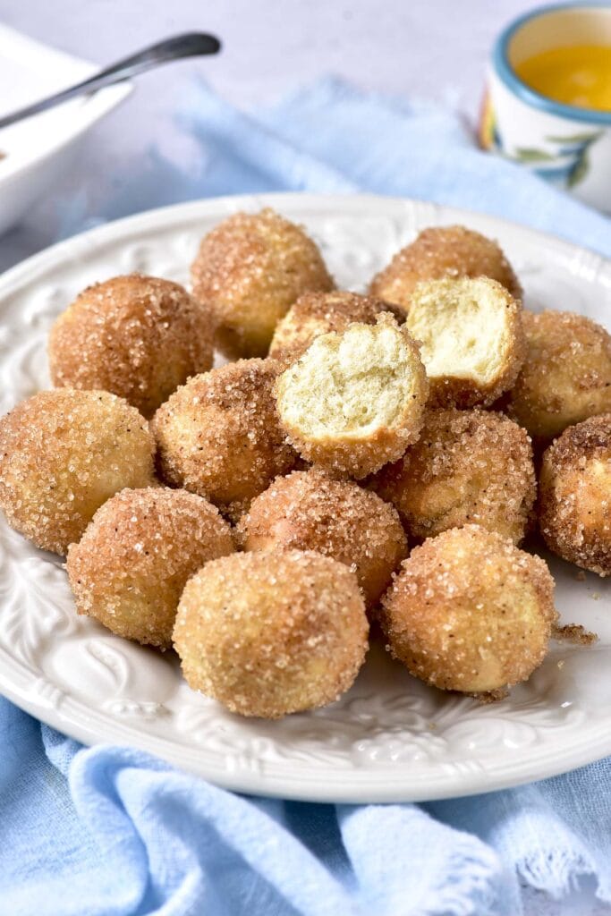 sugar coated donut holes covering a plate with blue cloth underneath.