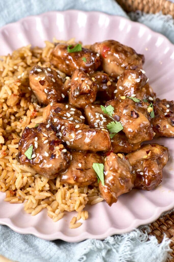 honey garlic chicken pieces covered in sesame seeds sitting on rice and pink plate.