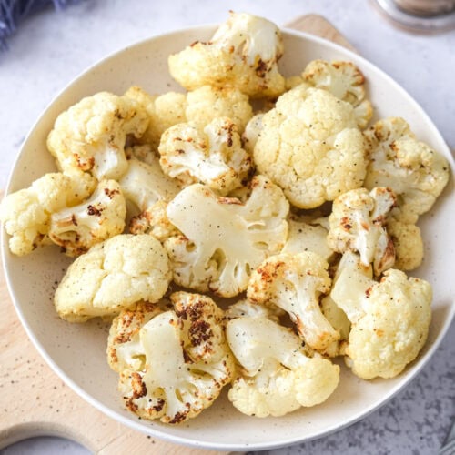 bowl of air fryer cauliflower on wooden board with cutlery beside.