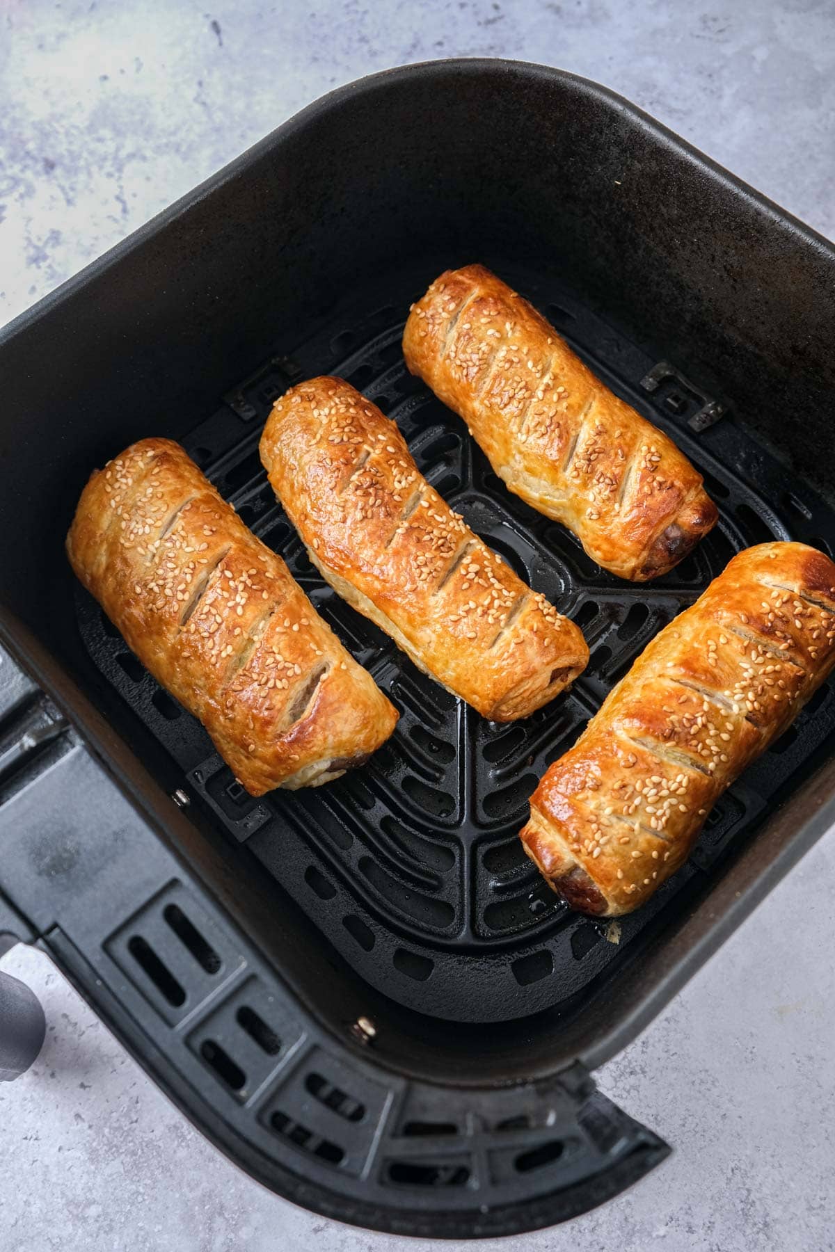 four cooked sausage rolls in air fryer tray.
