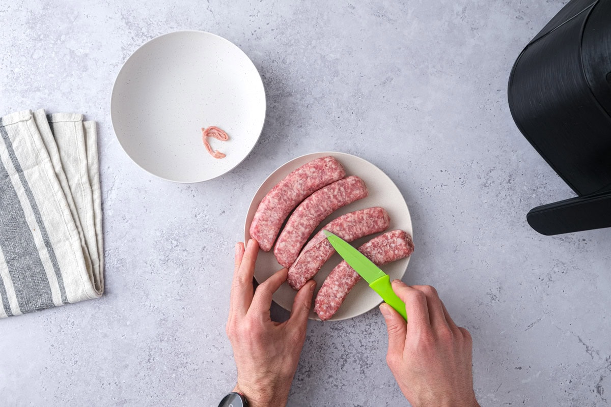 hand removing casings from sausages on plate on counter.