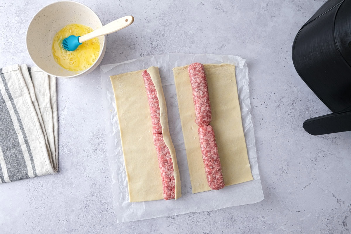puff pastry folded over one line of raw sausage on counter.