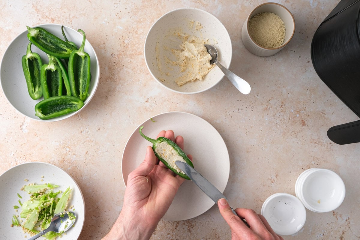 hand holding butter knife spreading cheesy filling into green pepper half.