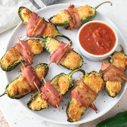 crispy jalapeno poppers wrapped in bacon on white plate.