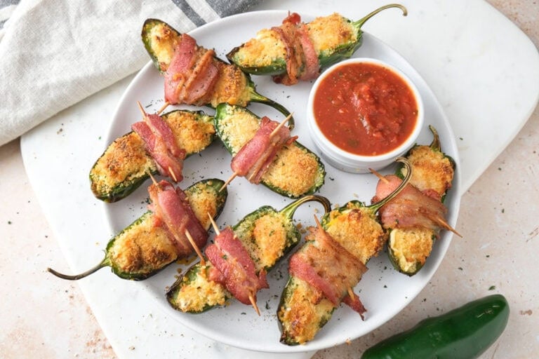 crispy jalapeno poppers wrapped in bacon on white plate.