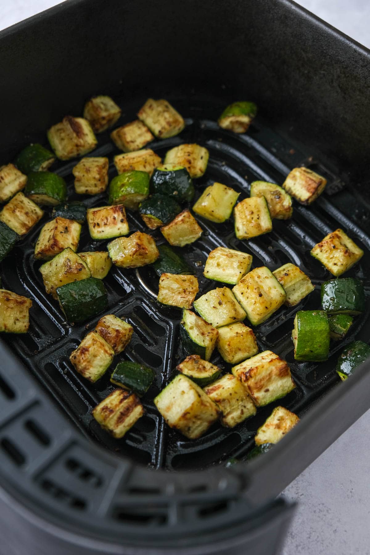 cooked zucchini pieces in air fryer basket.