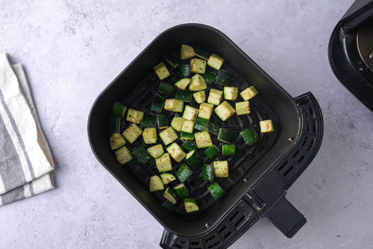 raw zucchini chunks in black air fryer basket.